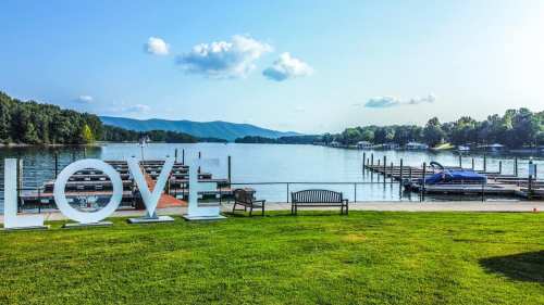 A serene lakeside view with a large "LOVE" sign, benches, and boats docked under a clear blue sky.