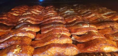 Rows of smoked salmon fillets with a rich, golden-brown glaze, arranged neatly in a smoker.