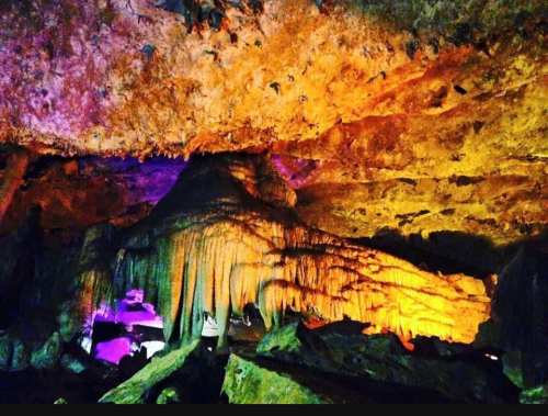 Colorful cave interior with dramatic rock formations and illuminated stalactites.