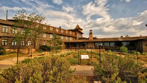 Historic lodge surrounded by greenery under a cloudy sky, featuring a stone chimney and wooden architecture.