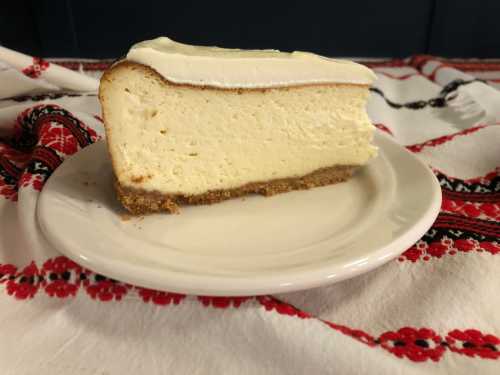 A slice of cheesecake on a small plate, resting on a decorative red and white patterned tablecloth.