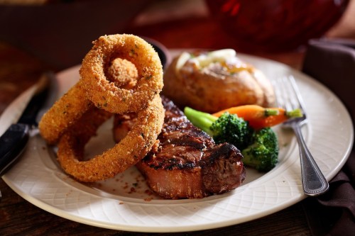 A plate featuring a juicy steak, crispy onion rings, a baked potato, and mixed vegetables.