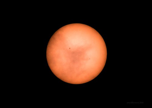 A bright orange sun partially obscured by clouds against a black background.