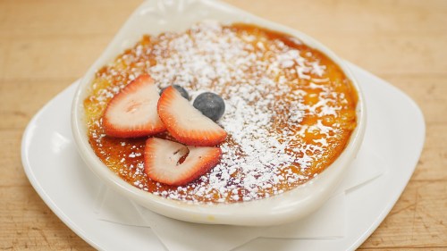 A creamy dessert topped with strawberries, blueberries, and powdered sugar in a white dish.