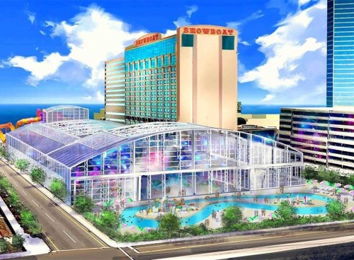 A colorful water park with a large glass structure, surrounded by greenery and a hotel in the background.