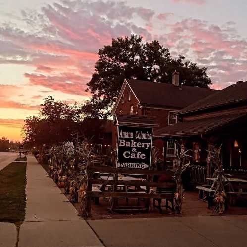 A bakery and café sign at sunset, surrounded by corn decorations and trees, with a colorful sky in the background.