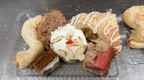 A variety of pastries on a clear plastic tray, including a cream-filled pastry, cake pieces, and cookies.