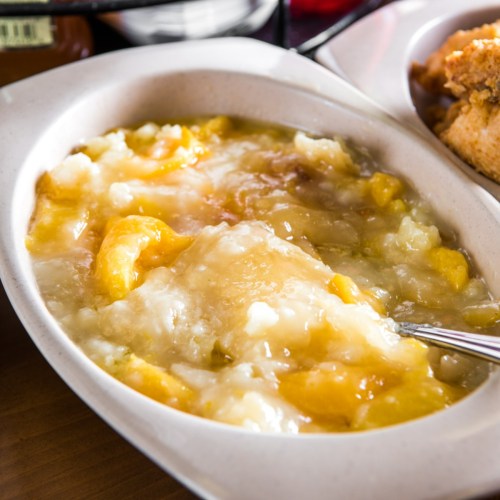 A dish of creamy, sweet fruit dessert with chunks of peaches and a glossy syrupy sauce.