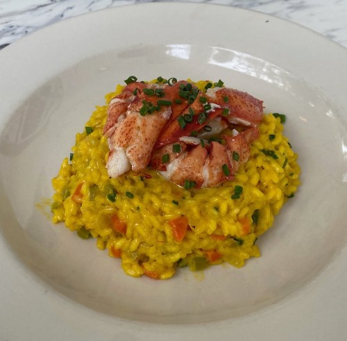A plate of vibrant yellow risotto topped with lobster meat and garnished with chopped chives.