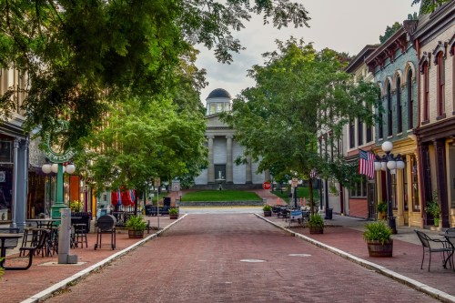 A charming street lined with trees and historic buildings, leading to a prominent building in the background.