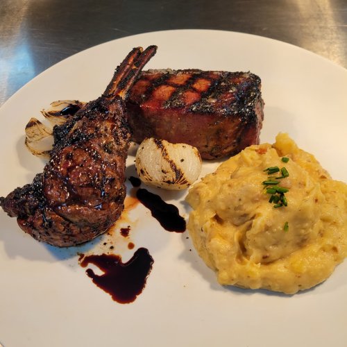 A plate featuring grilled lamb chops, a steak, and creamy mashed potatoes with chives, garnished with grilled onions.