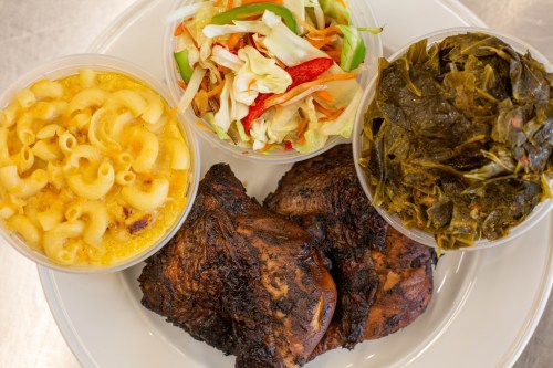 A plate featuring grilled chicken, macaroni and cheese, collard greens, and a fresh salad in separate containers.