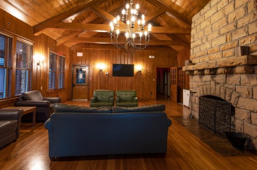Cozy wooden interior of a living room with a stone fireplace, chandelier, and comfortable seating.