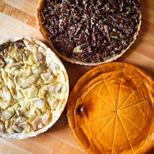 Three delicious pies on a wooden surface: apple, pecan, and pumpkin, each with a golden crust.