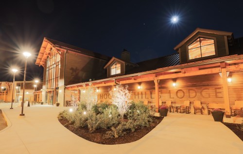A lodge exterior at night, featuring warm lighting, a landscaped entrance, and a bright moon in the sky.