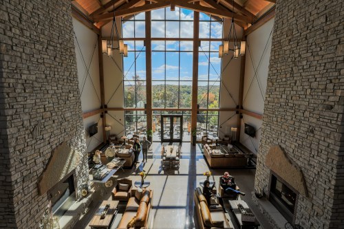 Spacious lodge interior with stone walls, large windows, and cozy seating, overlooking a scenic outdoor view.