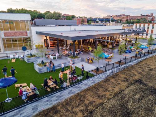 A rooftop venue with people socializing, dining, and playing games on a grassy area, surrounded by city buildings.
