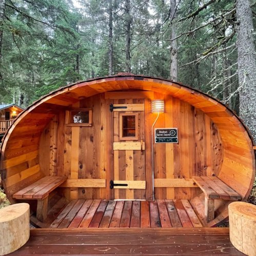 A cozy wooden sauna nestled among tall trees, featuring a round design and benches inside.