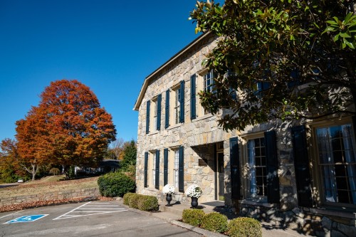 A stone building with large windows, surrounded by autumn trees and a clear blue sky.