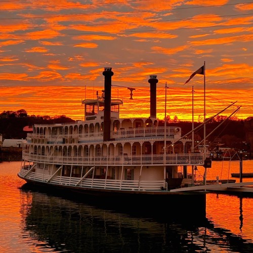 A paddleboat docked on water, silhouetted against a vibrant orange and purple sunset sky.