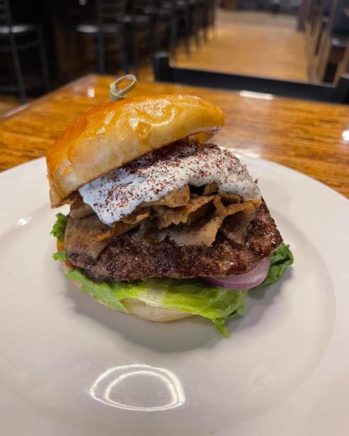 A stacked burger with a beef patty, lettuce, onion, and crispy toppings, served on a toasted bun.