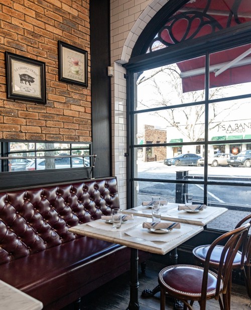 Cozy restaurant interior with a brick wall, tufted seating, marble table, and large windows overlooking the street.