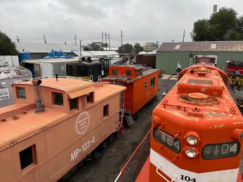 A view of vintage trains and cabooses in a rail yard under a cloudy sky.