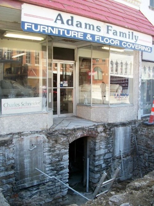 Storefront of "Adams Family Furniture" with exposed foundation and construction work visible in front.