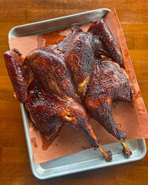 A beautifully smoked whole turkey on a tray, glistening with a rich, dark glaze.