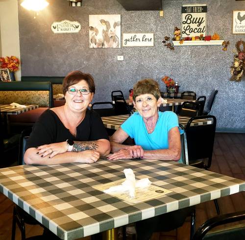 Two women sit at a checkered table in a cozy restaurant, smiling and enjoying each other's company.