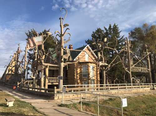 A unique log cabin with whimsical tree sculptures and an American flag, set against a blue sky.