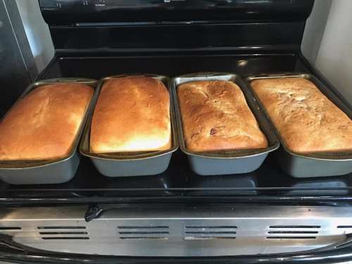 Four freshly baked loaves of bread in metal pans on a black stovetop.