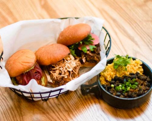 A basket with four mini burgers and a side of black beans and rice, garnished with cilantro.