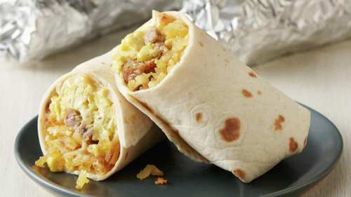 Two breakfast burritos filled with eggs, sausage, and potatoes, served on a plate with foil in the background.