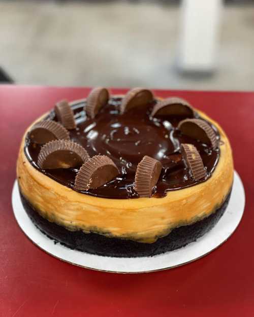 A chocolate cheesecake topped with chocolate ganache and peanut butter cups on a dark crust.