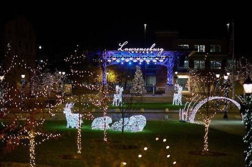 A festive park scene at night, featuring illuminated reindeer and trees, with a stage and "Lawrenceburg" sign in the background.