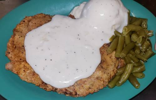 A plate of fried chicken topped with white gravy, served with green beans on the side.