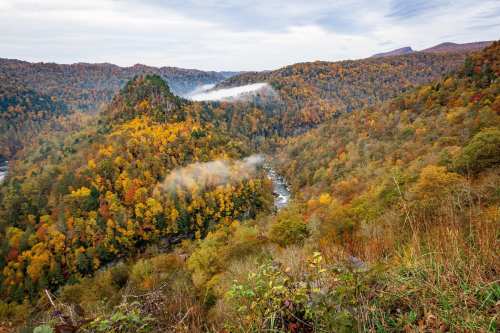A scenic view of rolling hills covered in autumn foliage, with mist rising over a river valley.