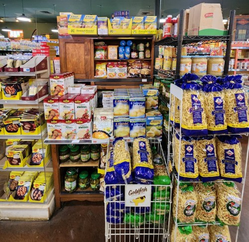 A grocery store display featuring various packaged foods, pasta, and canned goods on shelves and racks.