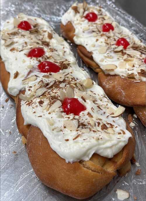 Two dessert pastries topped with whipped cream, sliced almonds, chocolate shavings, and cherries on a silver tray.