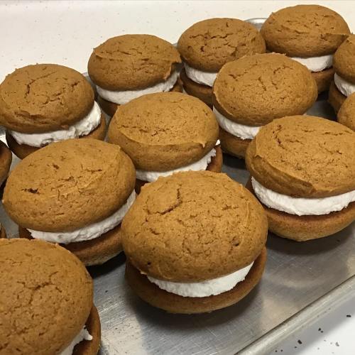 A tray of freshly made whoopie pies with pumpkin-colored cookies and white cream filling.