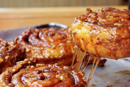 Close-up of gooey cinnamon rolls drizzled with caramel and topped with nuts, on a metal tray.
