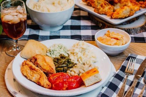A plate of fried chicken, green beans, mashed potatoes, cornbread, and tomatoes, with iced tea and biscuits in the background.