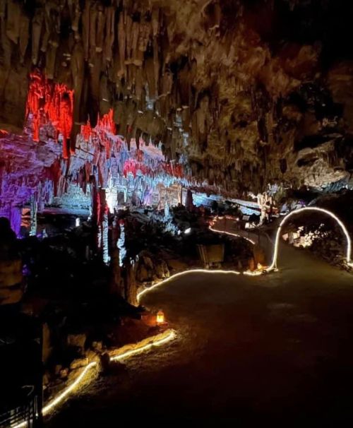 A dimly lit cave with colorful stalactites and stalagmites, featuring illuminated pathways and a mystical atmosphere.