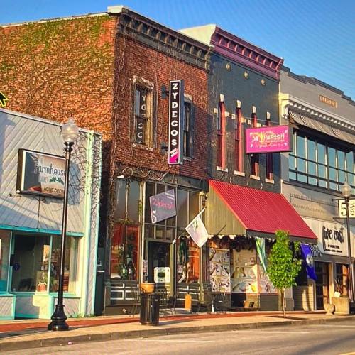 Colorful storefronts line a street, featuring signs for Zydeco's and a home decor shop, with greenery and lampposts.