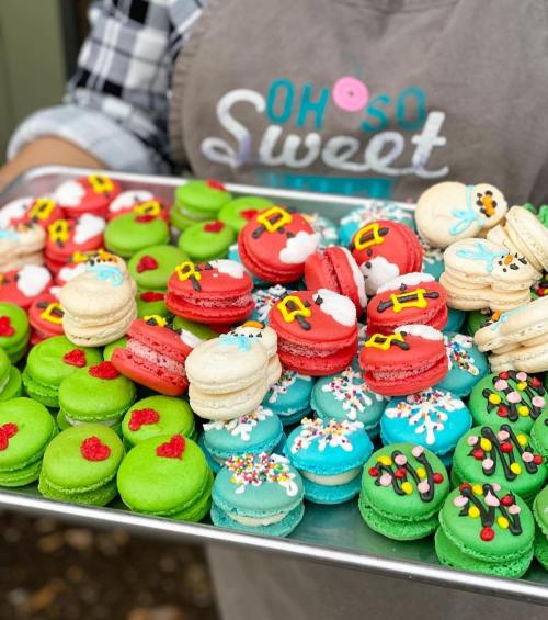 A tray of colorful macarons in festive designs, featuring red, green, blue, and white decorations for the holidays.