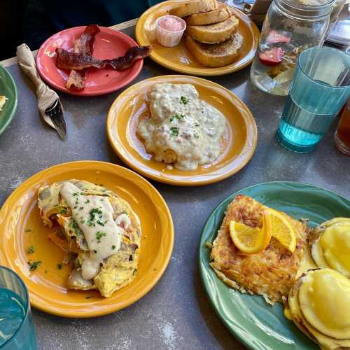 A colorful breakfast spread featuring omelet, biscuits with gravy, hash browns, bacon, and toast on vibrant plates.