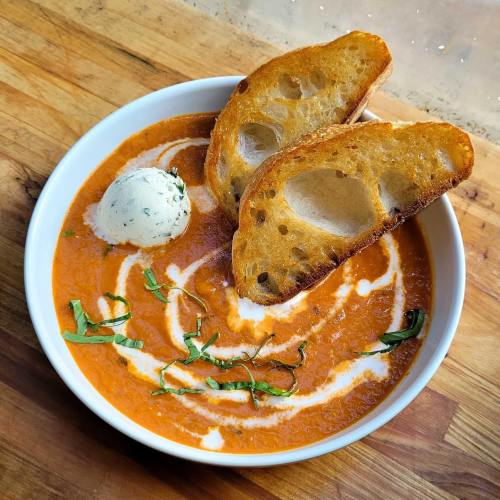 A bowl of creamy tomato soup topped with a dollop of herb butter and two slices of toasted bread on the side.