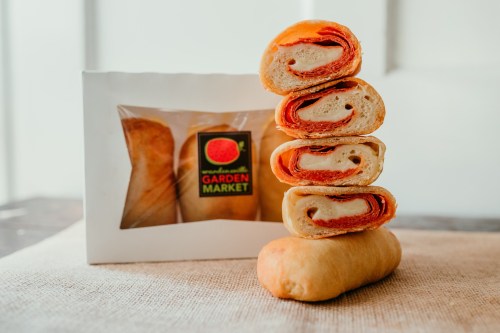 A stack of rolled pastries with layers of cheese and pepperoni, next to a box labeled "Garden Market."