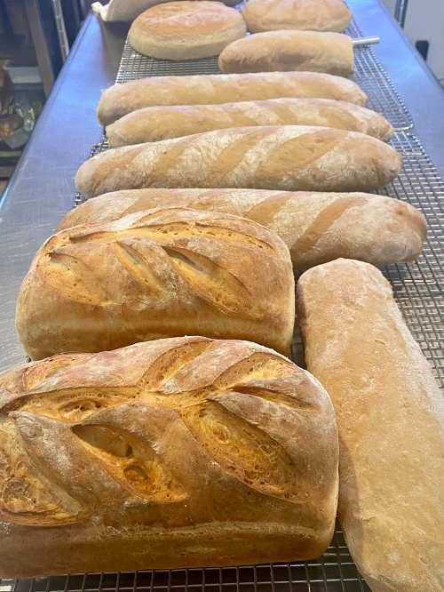 A variety of freshly baked loaves of bread cooling on a wire rack in a bakery.